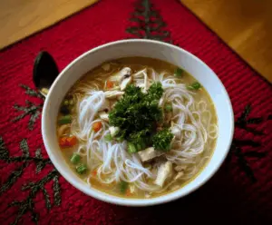 Hearty chicken rice noodle soup with tender chicken, fresh herbs, and colorful vegetables in a clear broth