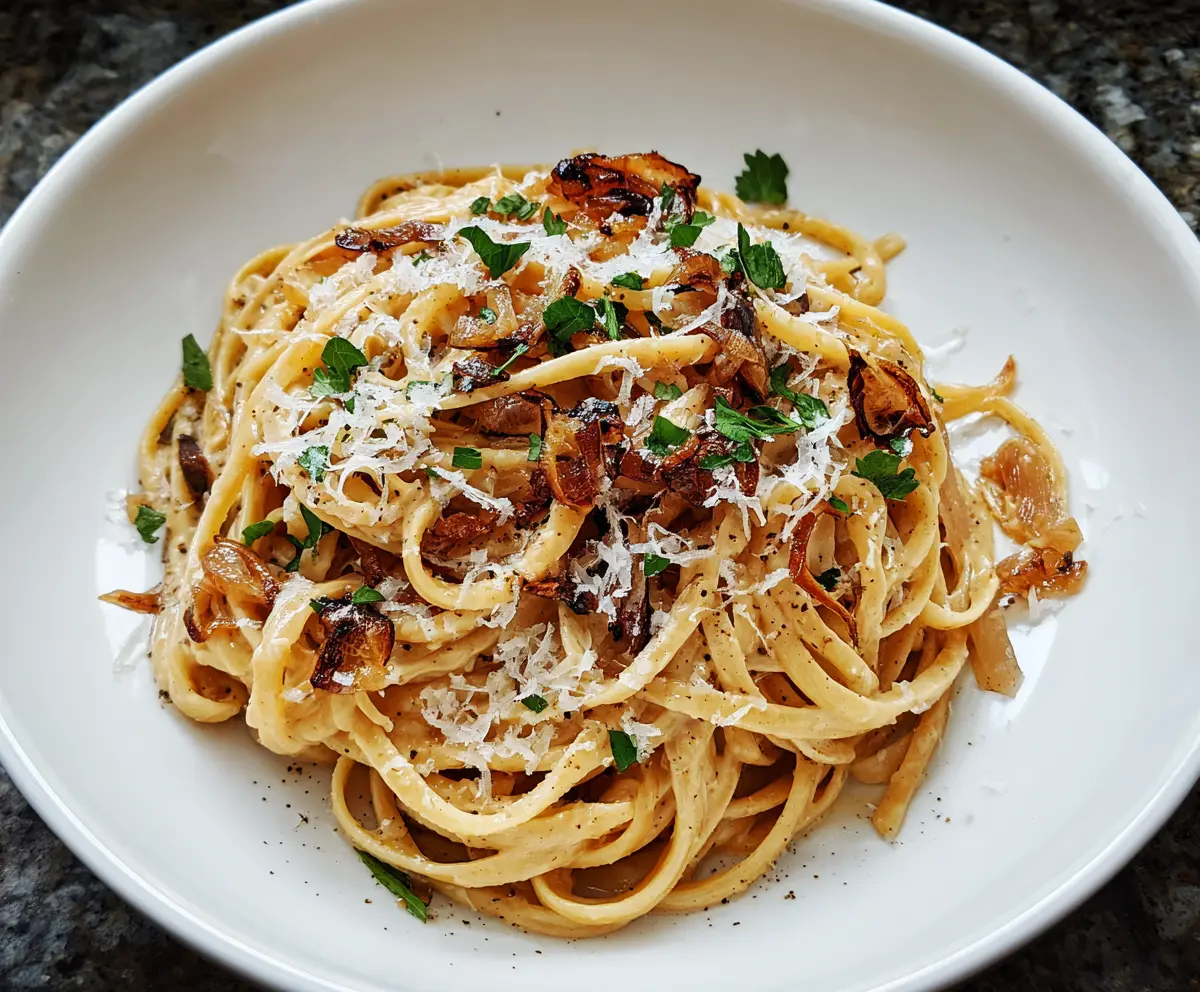 Delicious caramelized onion pasta served on a white plate, garnished with fresh herbs.