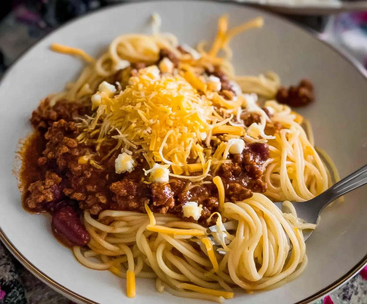 A delicious plate of Cincinnati chili spaghetti topped with shredded cheese and chopped onions.